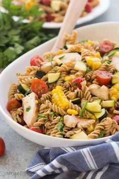 pasta salad with chicken, zucchini and tomatoes in a white bowl on a table