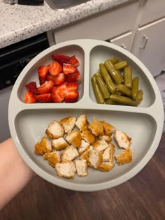 a person holding a plate with several different foods in it, including strawberries and green beans