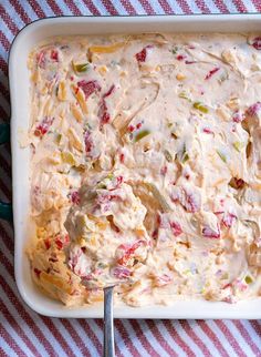 a casserole dish with cream cheese and vegetables in it on a red and white checkered table cloth