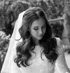 a woman in a wedding dress and veil holding a bouquet with her hand on the ground