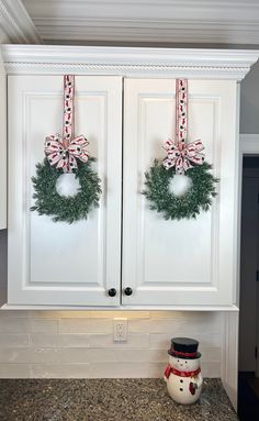 two christmas wreaths hanging on white cabinets