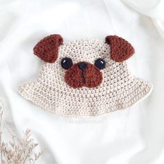 there is a crocheted dog face on the white blanket with brown ears and nose