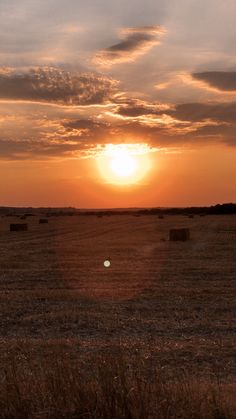 the sun is setting over a field with hay bales in the foreground and clouds in the background