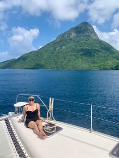 a woman sitting on the back of a boat in the ocean next to a mountain