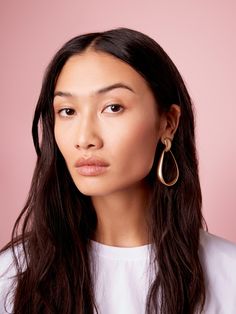 a woman with long dark hair wearing large gold hoop earrings and a white t - shirt