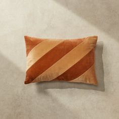 an orange and brown striped pillow laying on the floor in front of a white wall