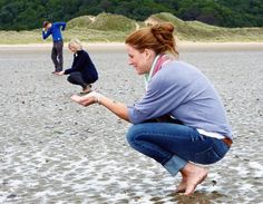 a woman kneeling down to pick up a bird from the water with another person in the background