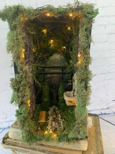 a small shrine with moss and lights on it's sides in front of a white brick wall