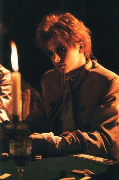 a young boy sitting at a table in front of a lit candle and looking down