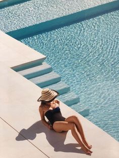 a woman sitting on the edge of a swimming pool wearing a hat and black bathing suit