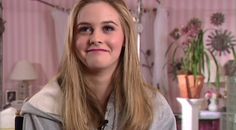 a woman with long blonde hair wearing a grey hoodie in a pink and white room