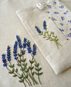 two embroidered napkins with blue flowers on them sitting next to each other, one in front of the other