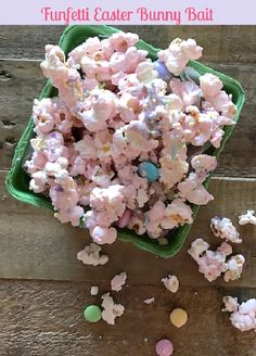 a green bowl filled with pink and white popcorn kernels on top of a wooden table