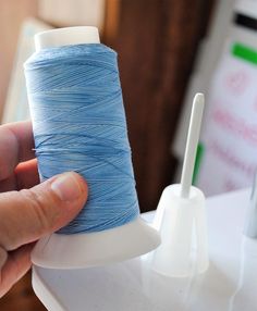 a hand is holding a spool of blue thread