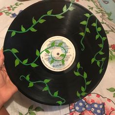 a hand holding a black record with green leaves painted on it and another hand reaching for the disc