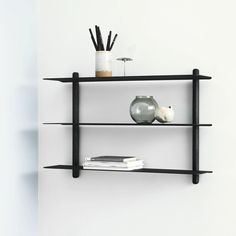 two black shelves with books and vases on them against a white wall in a room