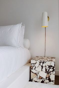 a white bed sitting next to a nightstand with a lamp on it