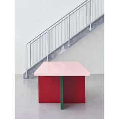 a pink and green table sitting in front of a stair case next to a red box