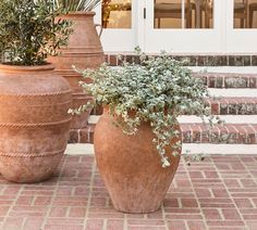 two large vases with plants in them sitting on the side of a brick building