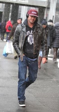 a man walking down the street in the rain wearing headphones and a leather jacket