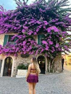 a woman standing in front of a building with purple flowers on it