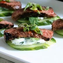 some meat and cucumbers are on a white platter with green peppers in the foreground