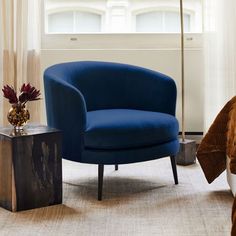 a blue chair sitting in a bedroom next to a lamp on a table with a vase