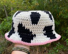 a woman's hand wearing a crocheted hat with black and white cow pattern