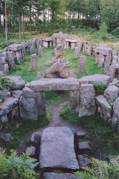 an old stone structure in the middle of a field with rocks and plants around it