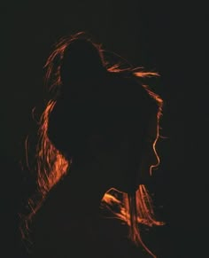 the silhouette of a woman's head against a dark background with light coming through her hair