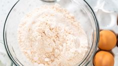 eggs and flour in a glass bowl on a white counter top next to other ingredients