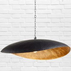 a large black and gold pendant light hanging from a chain against a white brick wall