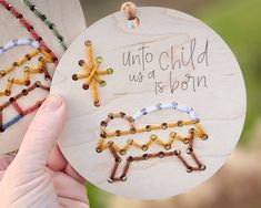 a person holding up a wooden ornament with bead designs on it that says unto child, us a born