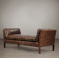 a brown leather chaise lounger sitting on top of a hard wood floor next to a white wall