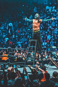 a man standing on top of a ladder in front of an audience at a wrestling match