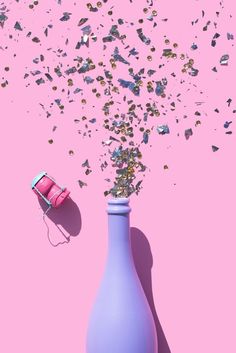 a purple vase with confetti spilling out of it on a pink surface next to a phone