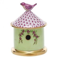 a green birdhouse with pink flowers on it's roof and a gold base