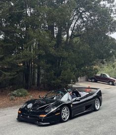 a black sports car is parked on the side of the road in front of some trees