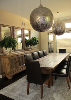 a dining room table with black leather chairs and two large round hanging lights above it