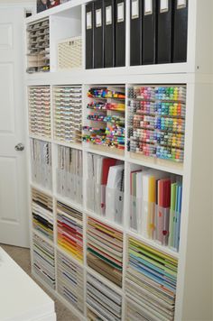 a white bookcase filled with lots of crafting supplies next to a wall full of file folders