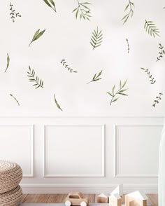 a room with white walls and green leaves on the wall, along with wooden toys