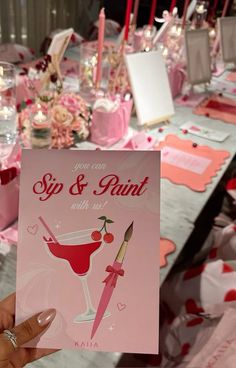 a person holding up a card for a sip and paint party with pink decorations on the table