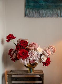 a vase filled with red and white flowers on top of a wooden table next to a painting