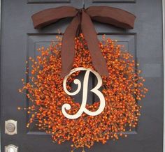 a wreath with the letter b on it is hanging on a front door and has a brown bow