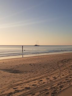 a boat is out in the water at sunset on a beach with footprints in the sand