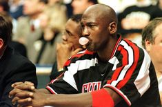 a man blowing bubbles in his mouth while sitting next to another man at a basketball game