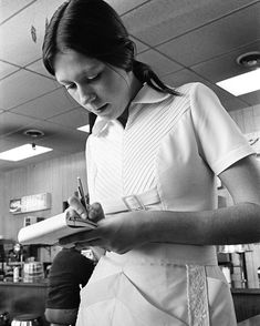 a woman in an apron writing on a piece of paper