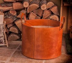 a large brown leather bucket sitting on top of a tile floor next to firewood