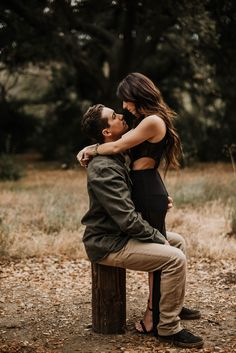 a man and woman kissing while sitting on a wooden post