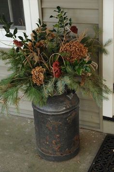 a metal bucket filled with flowers and greenery next to a door mat on the ground